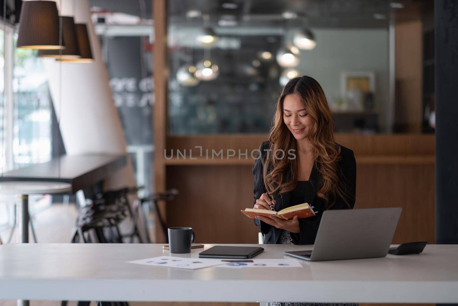 Happy asian business woman working on laptop computer and taking notes at the office.