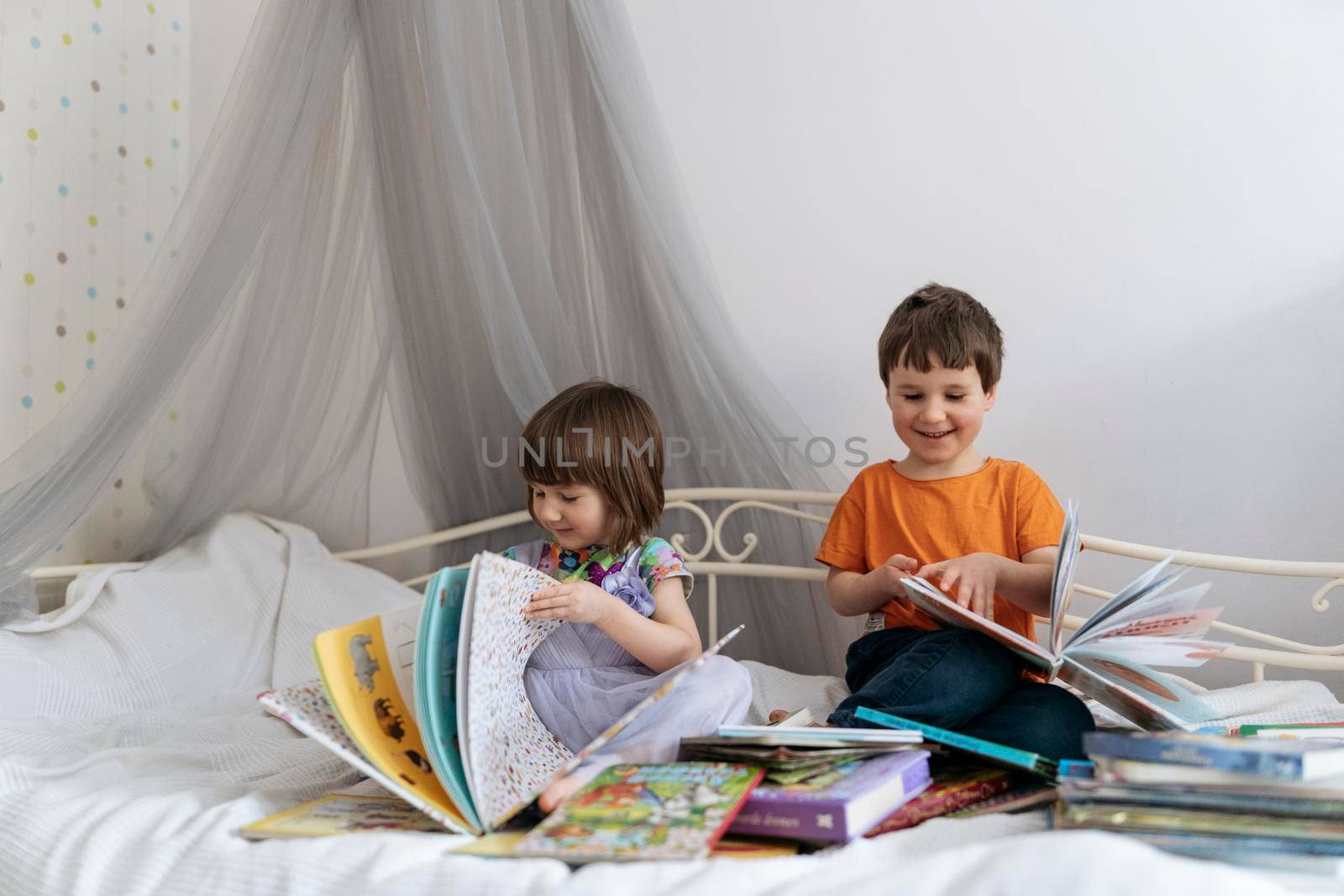 Two siblings reading books on the sofa and laughing together by Varaksina