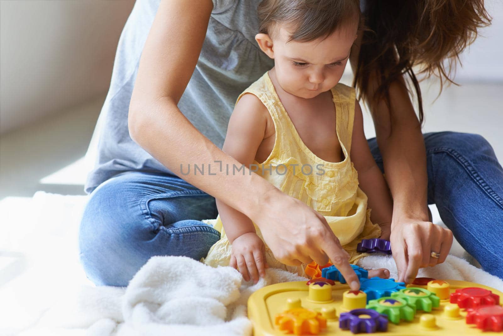 Learning with mom. Shot of a cute baby girl sitting on the floor with her mom and playing with toys. by YuriArcurs