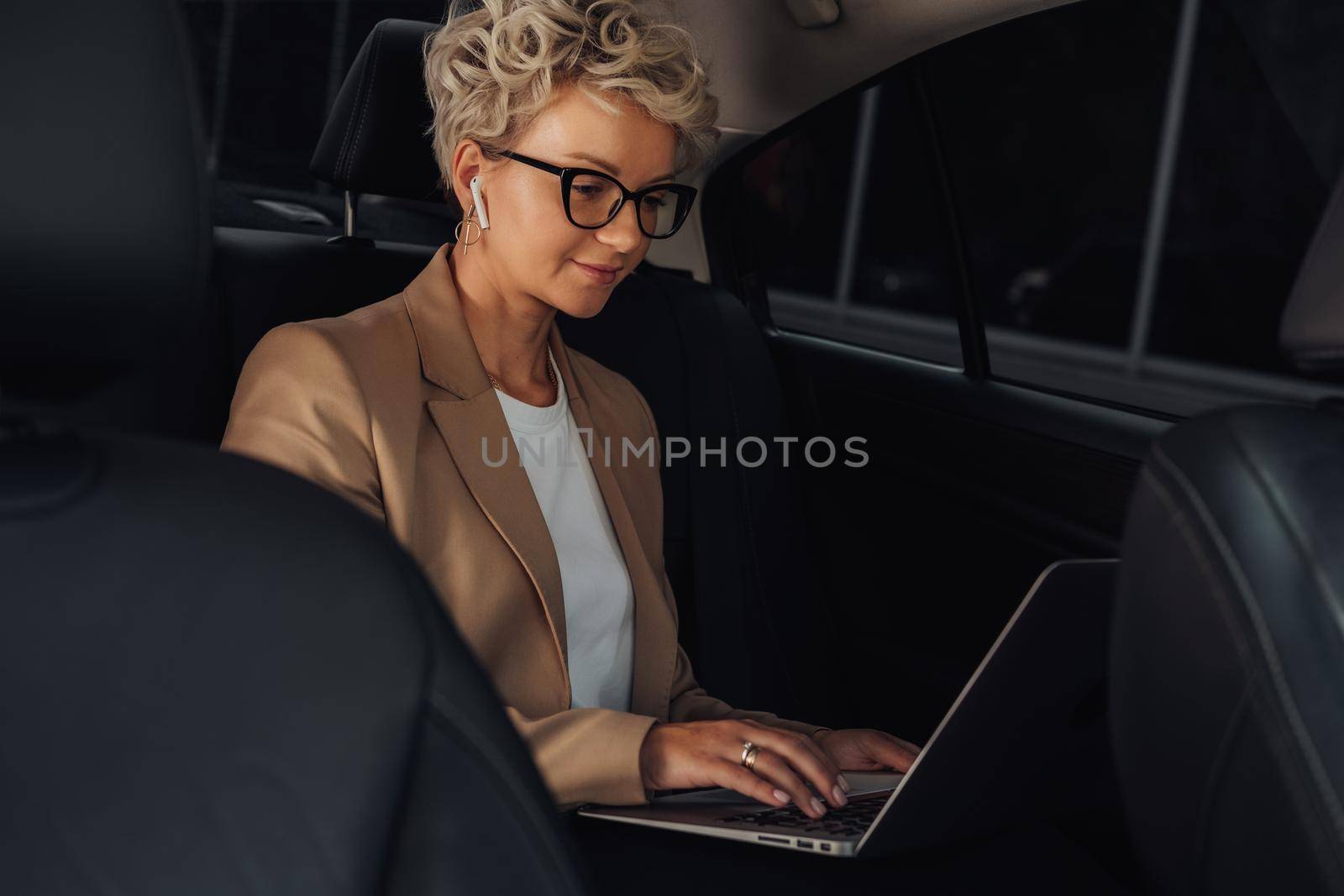 Stylish Business Woman Working on Laptop While Sitting on Back Seat of a Car by Romvy