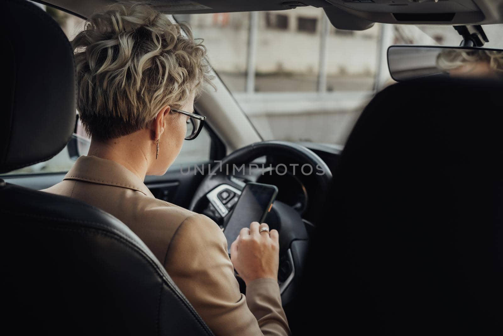 Business Woman Using a Smartphone While Driving Car, View from Back Seat by Romvy