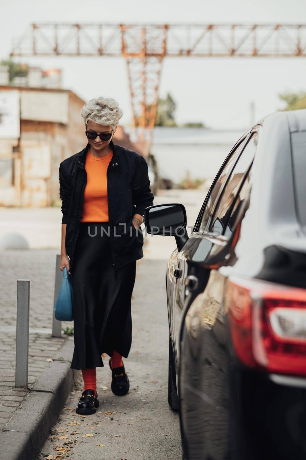 Stylish Young Woman in Jacket and Sunglasses Moving Near Black Car