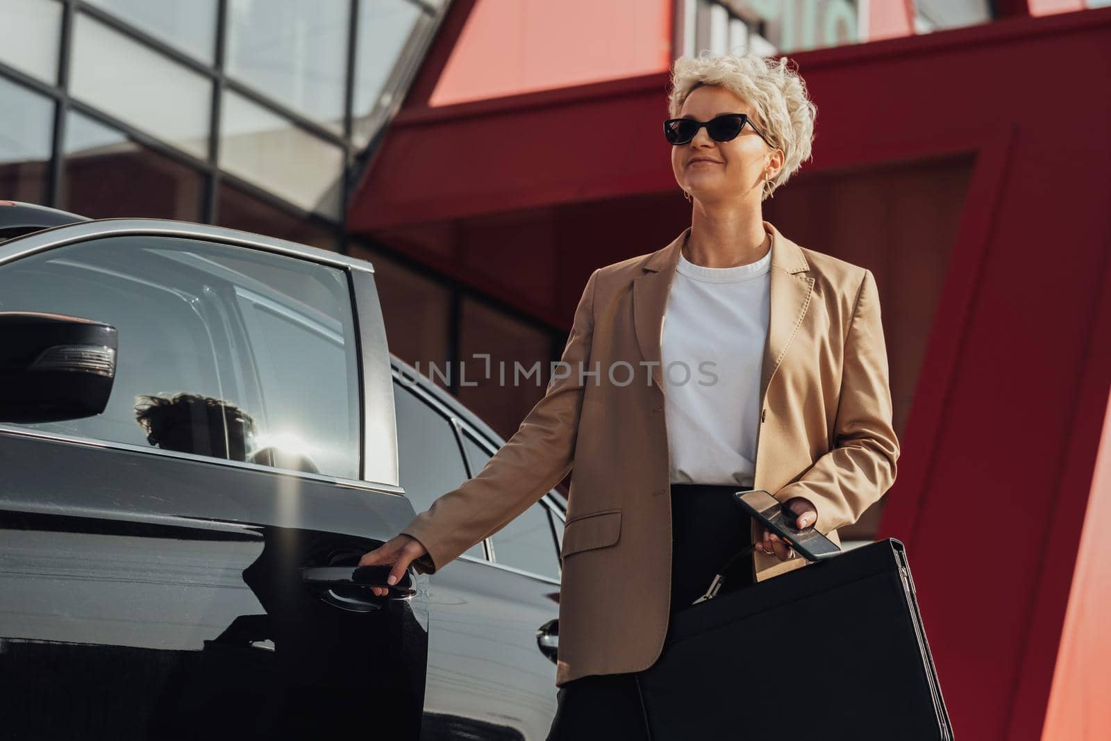 Elegant Female Entrepreneur with Briefcase in Hand Opening Door of the Luxury Car by Romvy