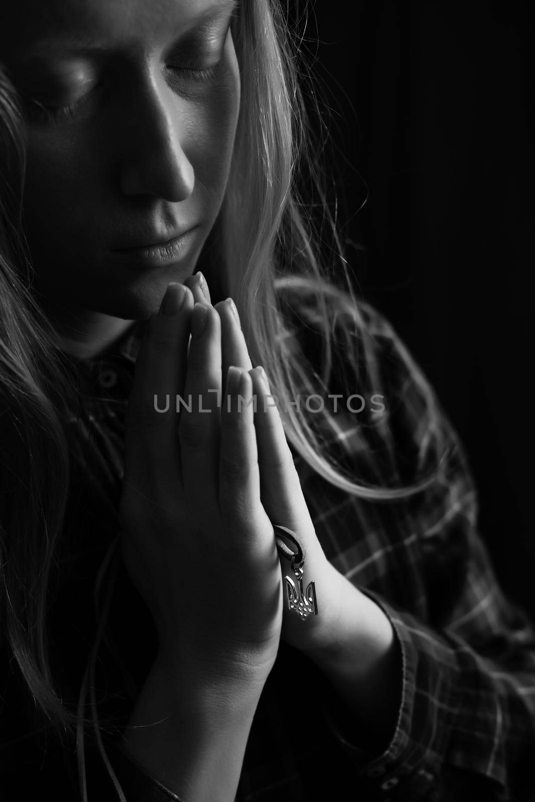 Ukrainian blonde woman prays for Ukraine during the war with the national emblem Trident in the palms close up. Russia attacked Ukraine on 2022. Black and white vertical photo