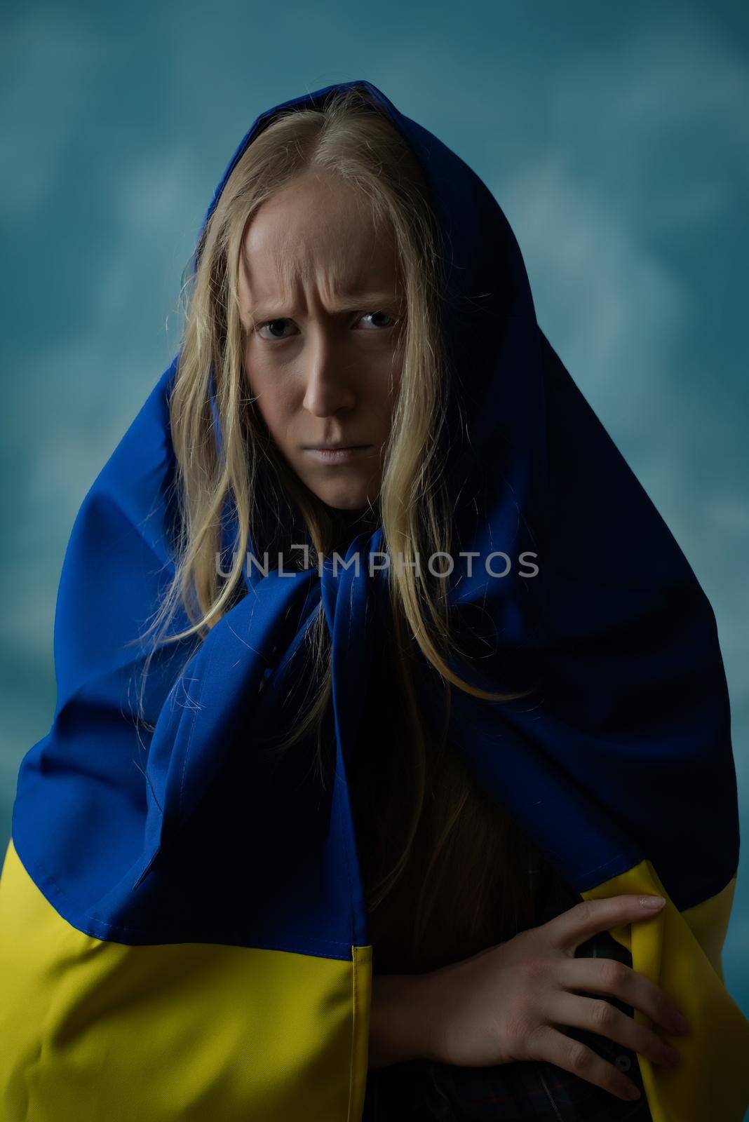 A real Ukrainian blonde woman is upset by evil and disappointed during the war with the state yellow and blue Ukrainian flag on her head. Russia attacked Ukraine on February 24, 2022.