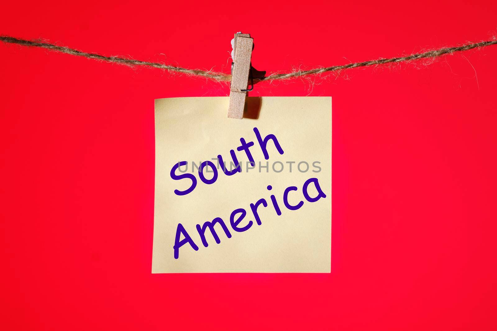 Phrase South America on a yellow sticker on a rope with clothespins on a red background..