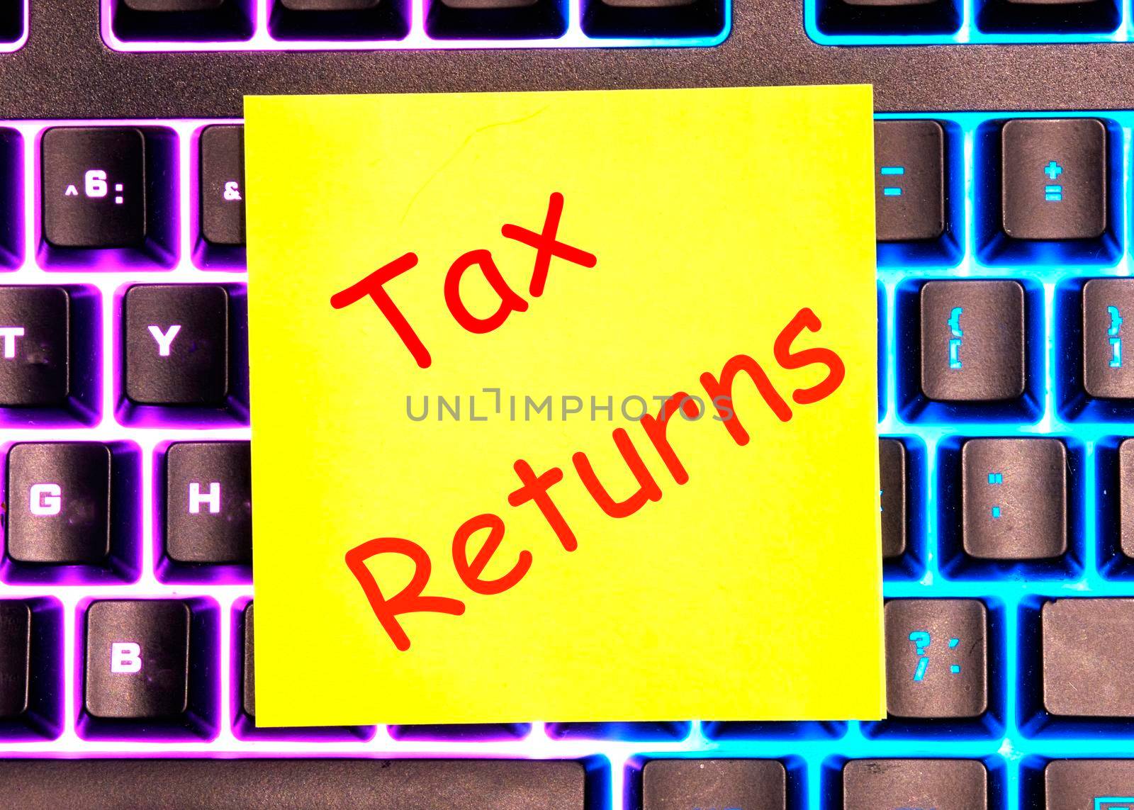 tax returns text written on a yellow sticker lies on a glowing keyboard.