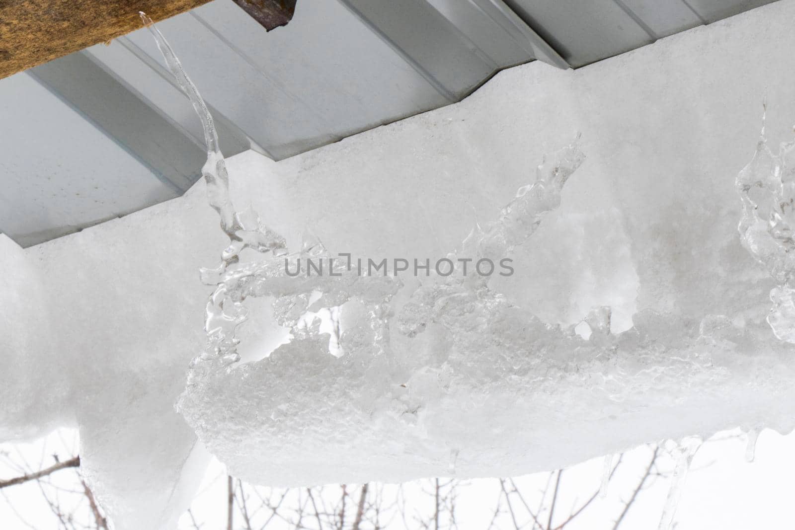 Icicles on the roof, white sky and iced water, winter ice