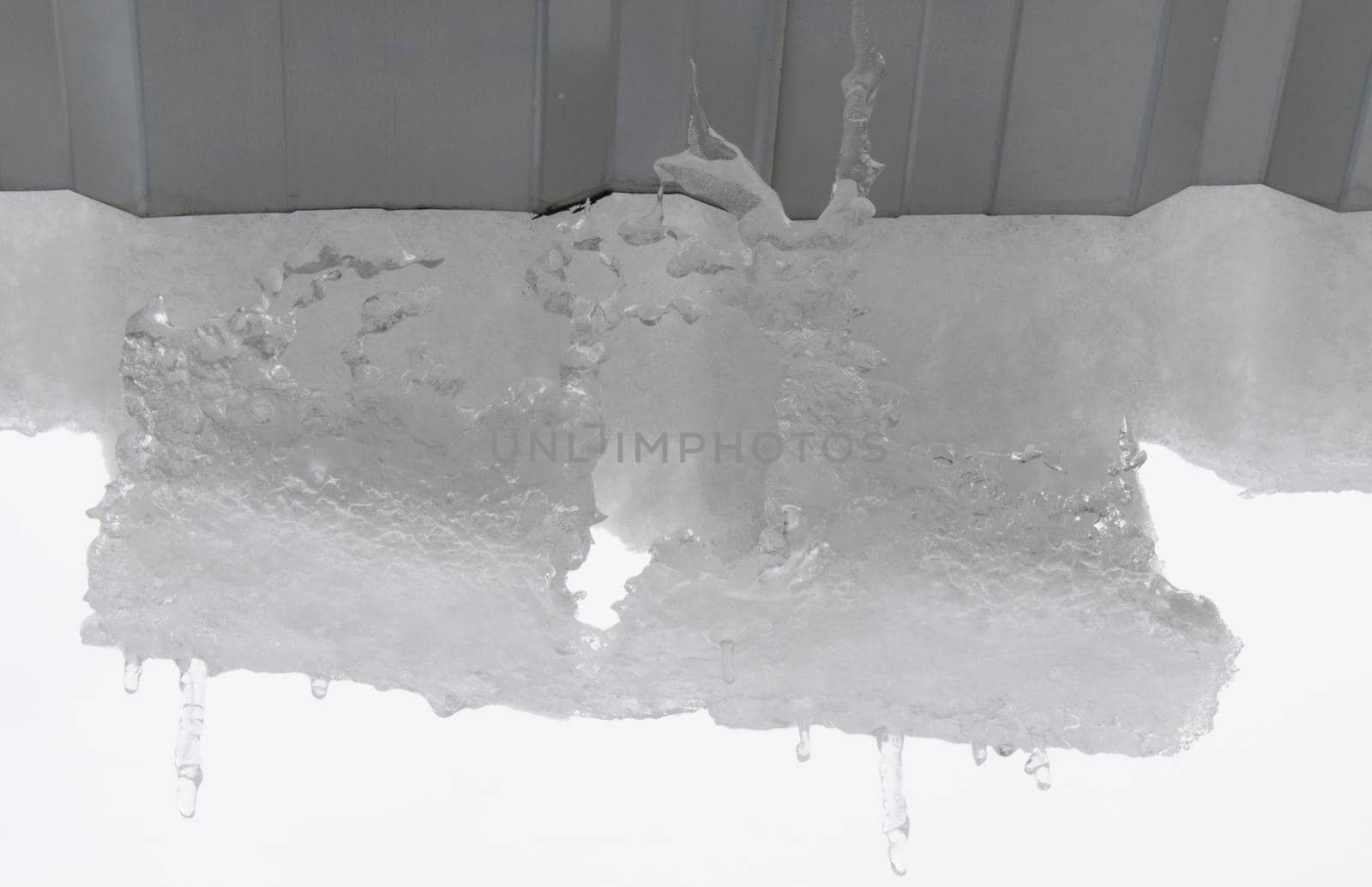 Icicles on the roof, white sky and iced water, winter ice