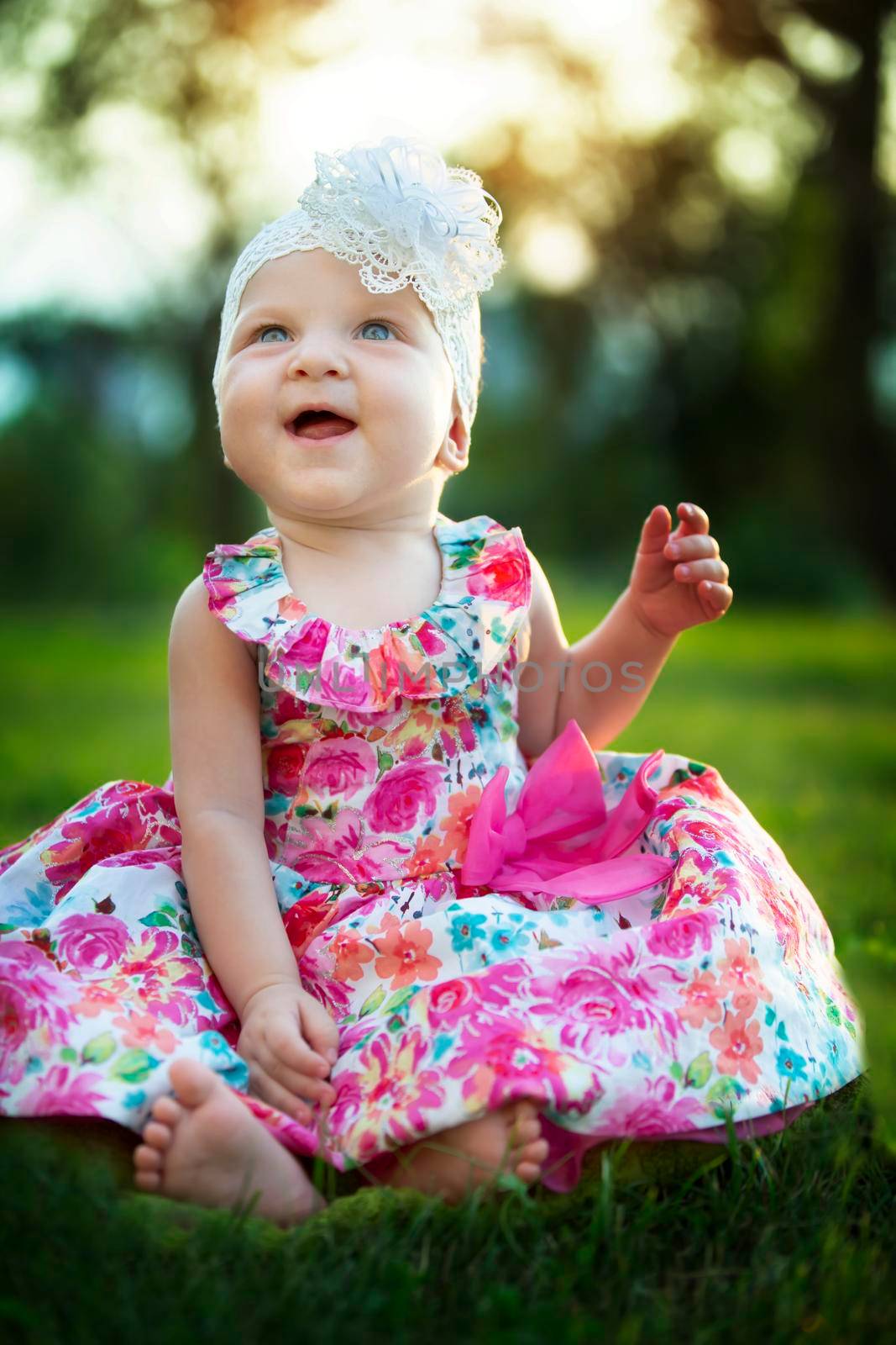 Happy little girl sits on the grass and laughs. Beautiful child. Little baby up to a year old on a summer meadow.