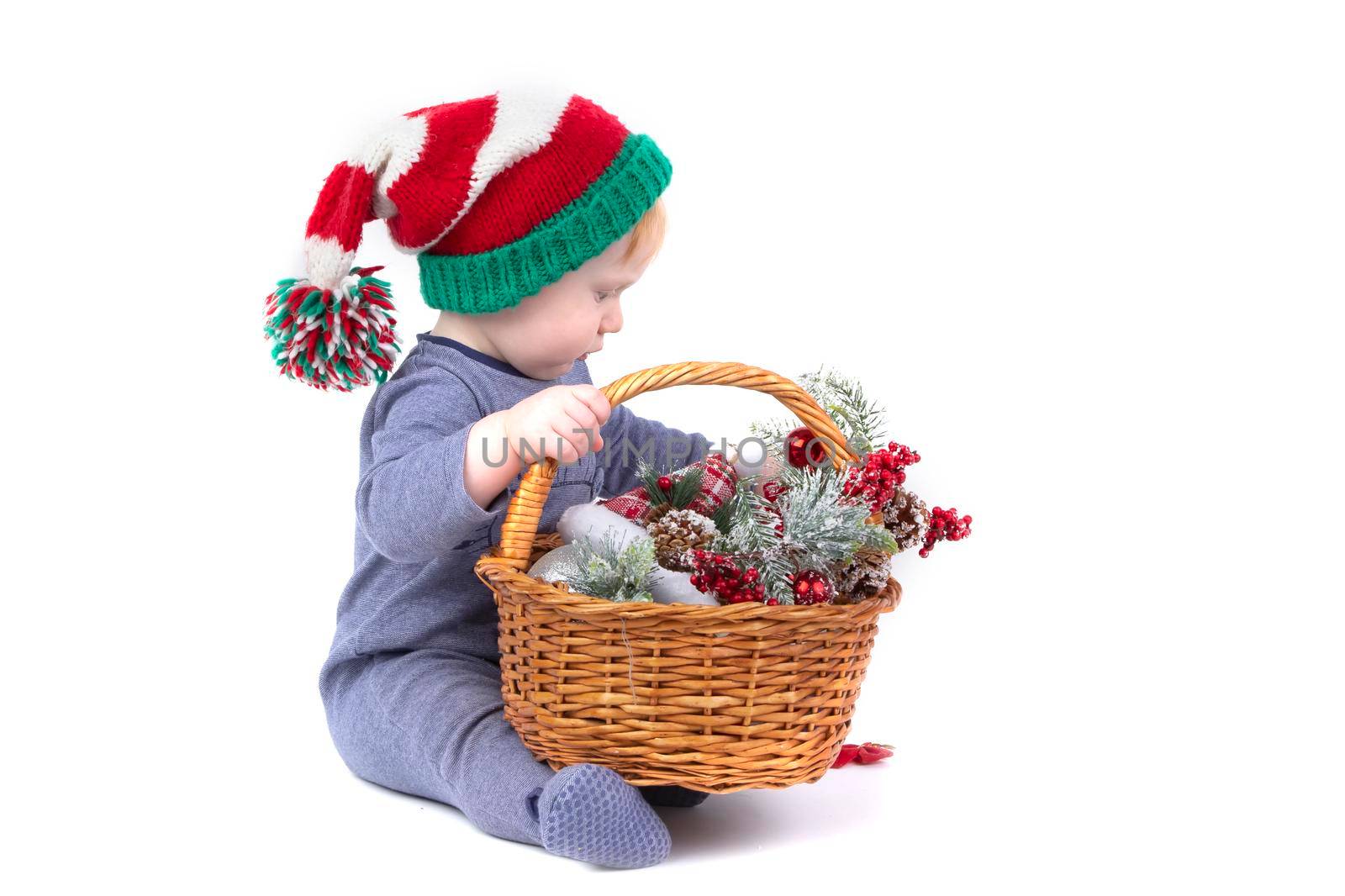 Kid in a Christmas hat with a basket of Christmas toys on a white background.