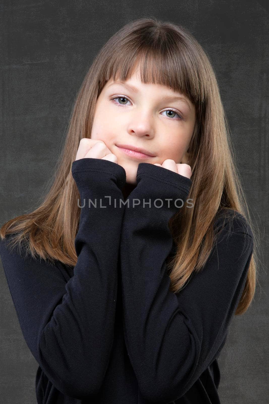 Portrait of a beautiful pensive girl of ten years old on a gray background.