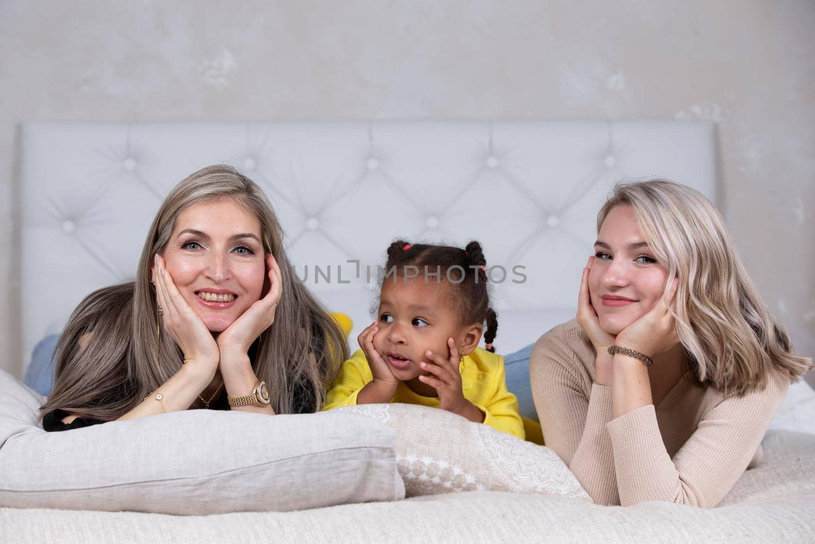 Family from different races. Mom grandmother light-skinned and a little African American girl lie on the sofa.