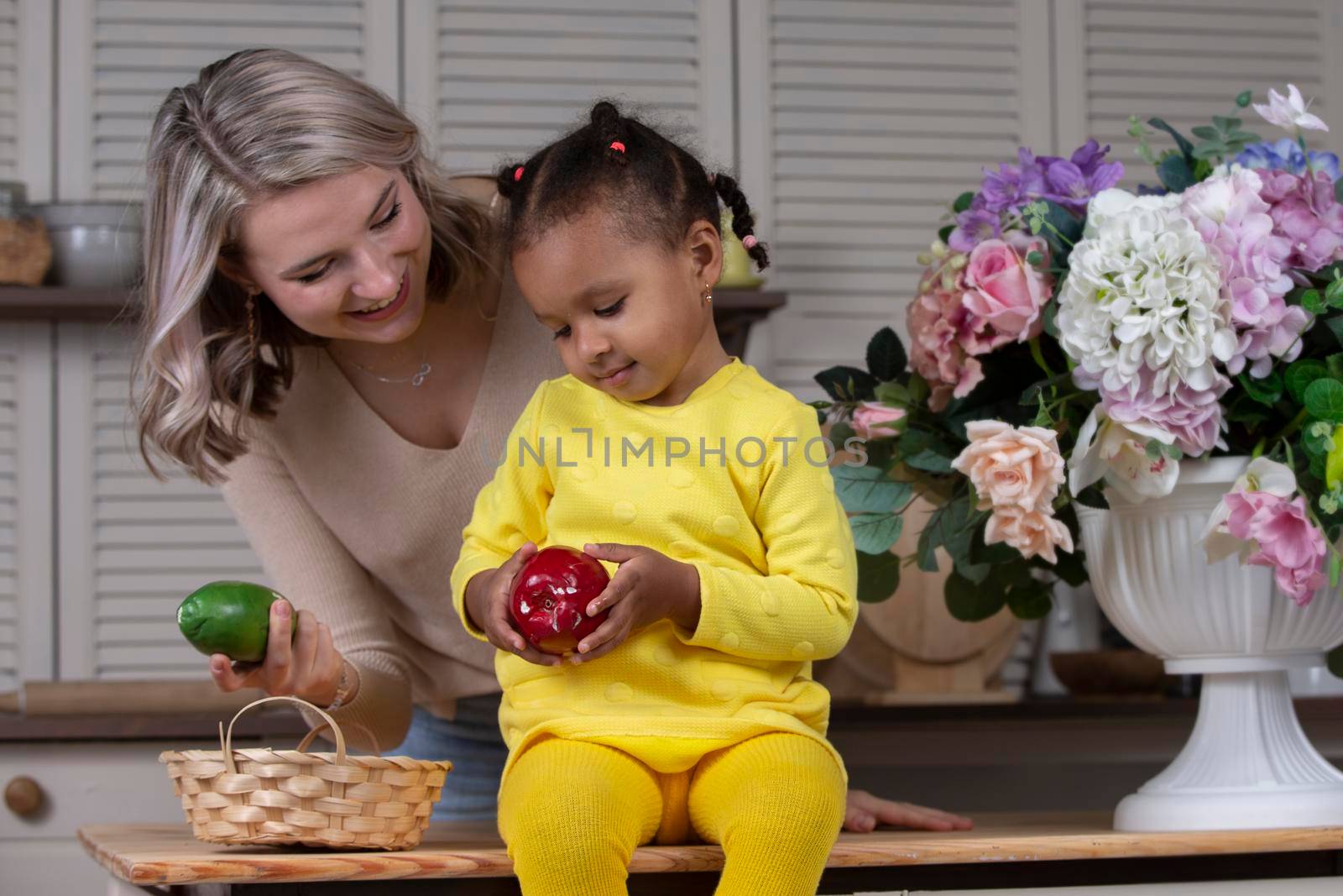 Multiethnic mom and daughter play at home in the kitchen. Cheerful mother with little daughter of African nationality. Family from different races.