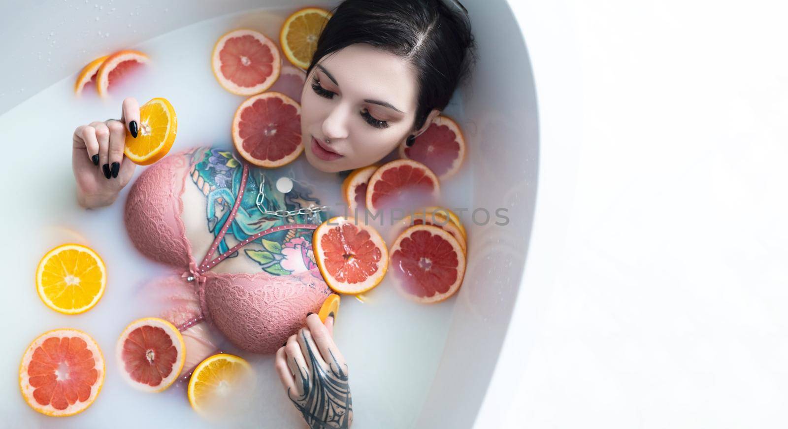 naked girl with tattoos takes a vitamin bath with sliced oranges and grapefruits
