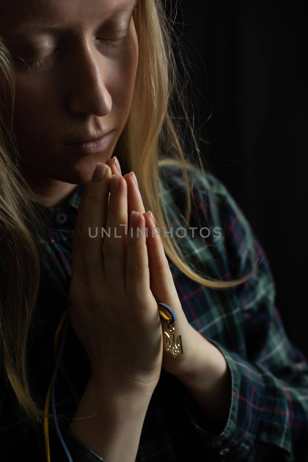 Ukrainian blonde woman prays for Ukraine during the war with the national emblem Trident in the palms close up. Russia attacked Ukraine on February 24, 2022