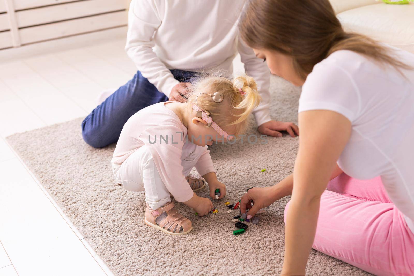 Baby child with hearing aids and cochlear implants plays with parents on floor. Deaf and rehabilitation