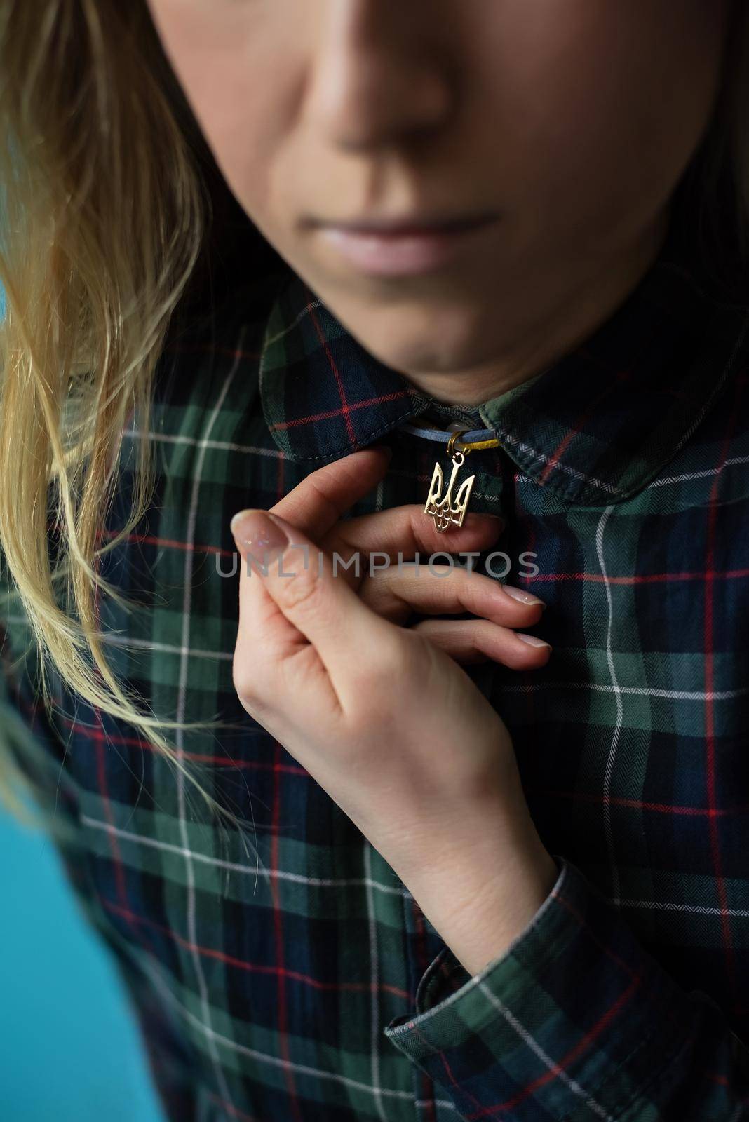 Ukrainian young blonde woman holding a pendant with the state emblem of Ukraine - Trident close up. Russia attacked Ukraine on February 24, 2022