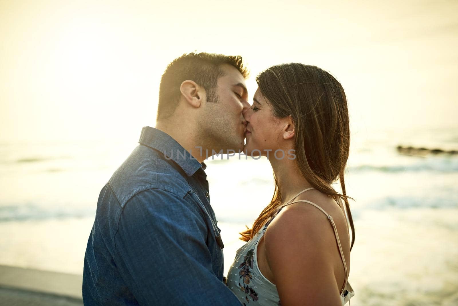 Cropped shot of an affectionate young couple kissing while standing on the beach.