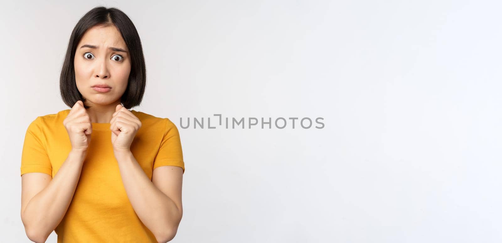 Portrait of scared asian woman shaking from fear, looking terrified and concerned, standing anxious against white background.