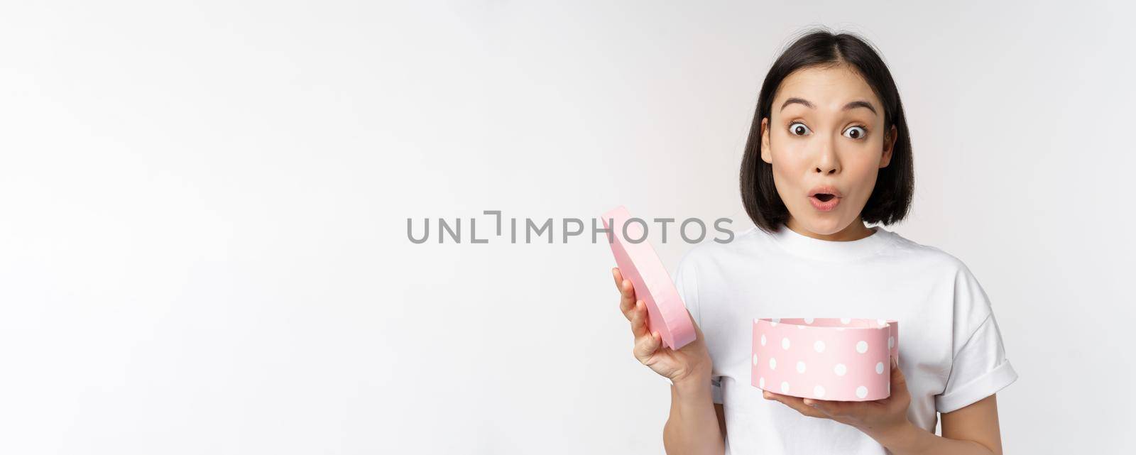 Happy asian woman, girlfriend open box with valentines day gift, receive romantic present, standing over white background. copy space