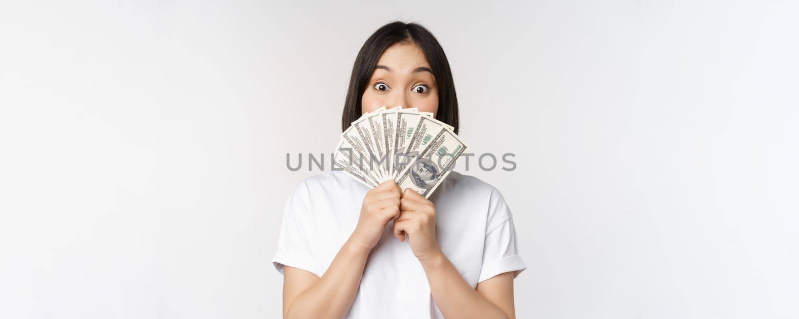 Happy asian girl holding money, cash near face, concept of microcredit and finance, white studio background. Copy space