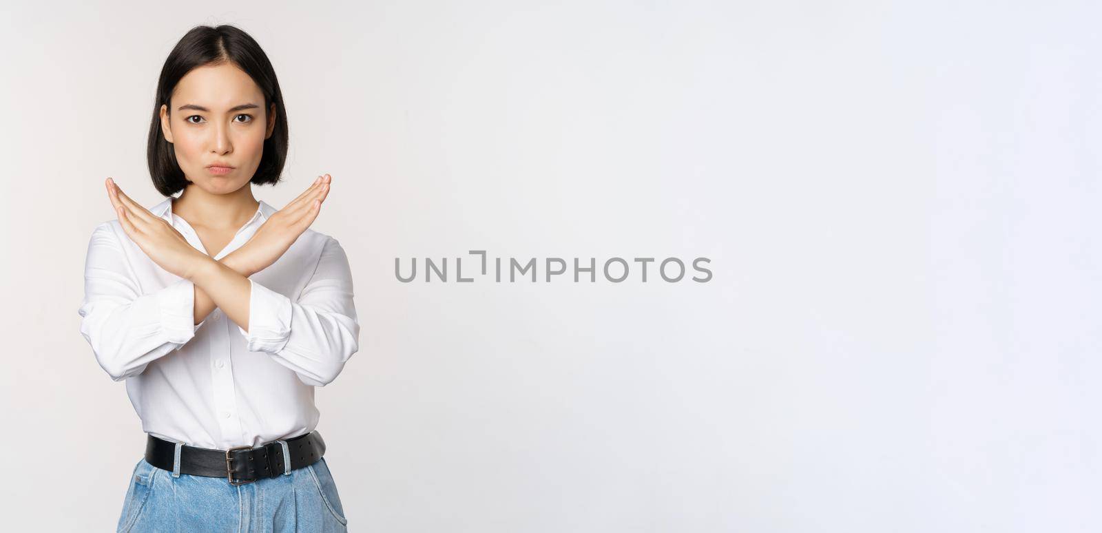 Image of young asian, korean girl student showing stop, cross prohibition sign, forbid smth, refusing, standing over white background by Benzoix