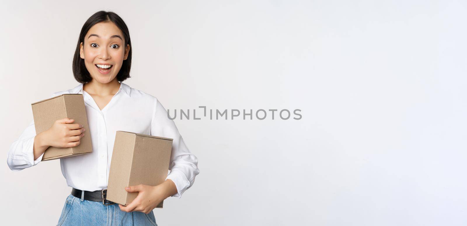 Portrait of happy korean girl holding two boxes and smiling, lookng amazed at camera, concept of shopping, white background.
