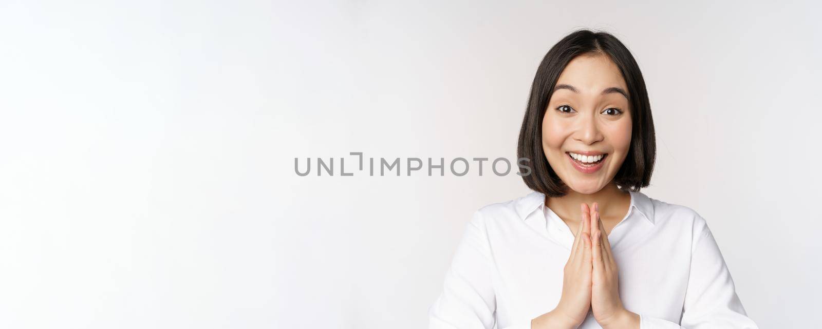 Close up portrait of young japanese woman showing namaste, thank you arigatou gesture, standing over white background.