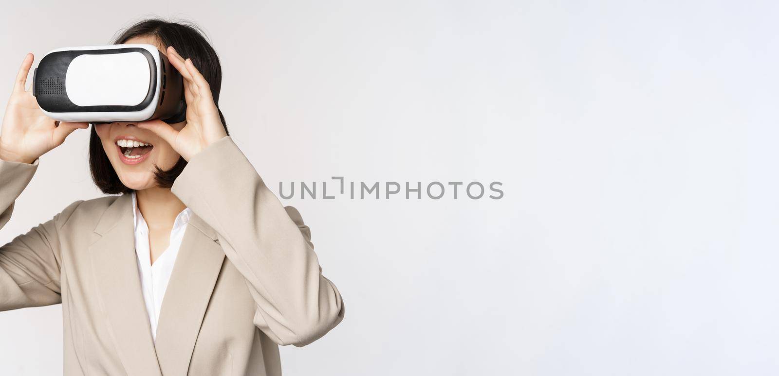Amazed business woman in suit using virtual reality glasses, looking amazed in vr headset, standing over white background by Benzoix