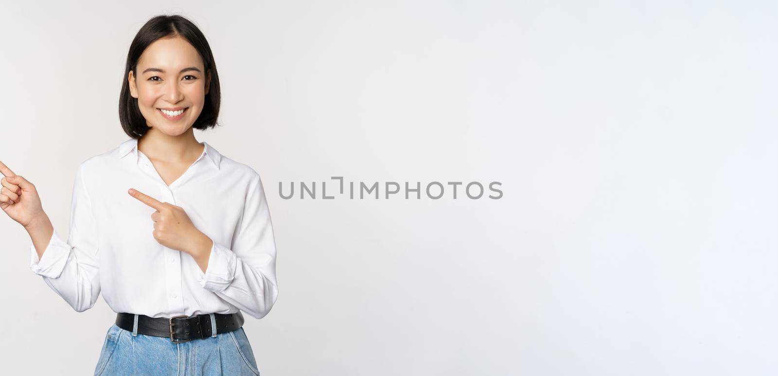 Image of smiling young office lady, asian business entrepreneur pointing fingers left, showing client info, chart of banner aside on copy space, white background.