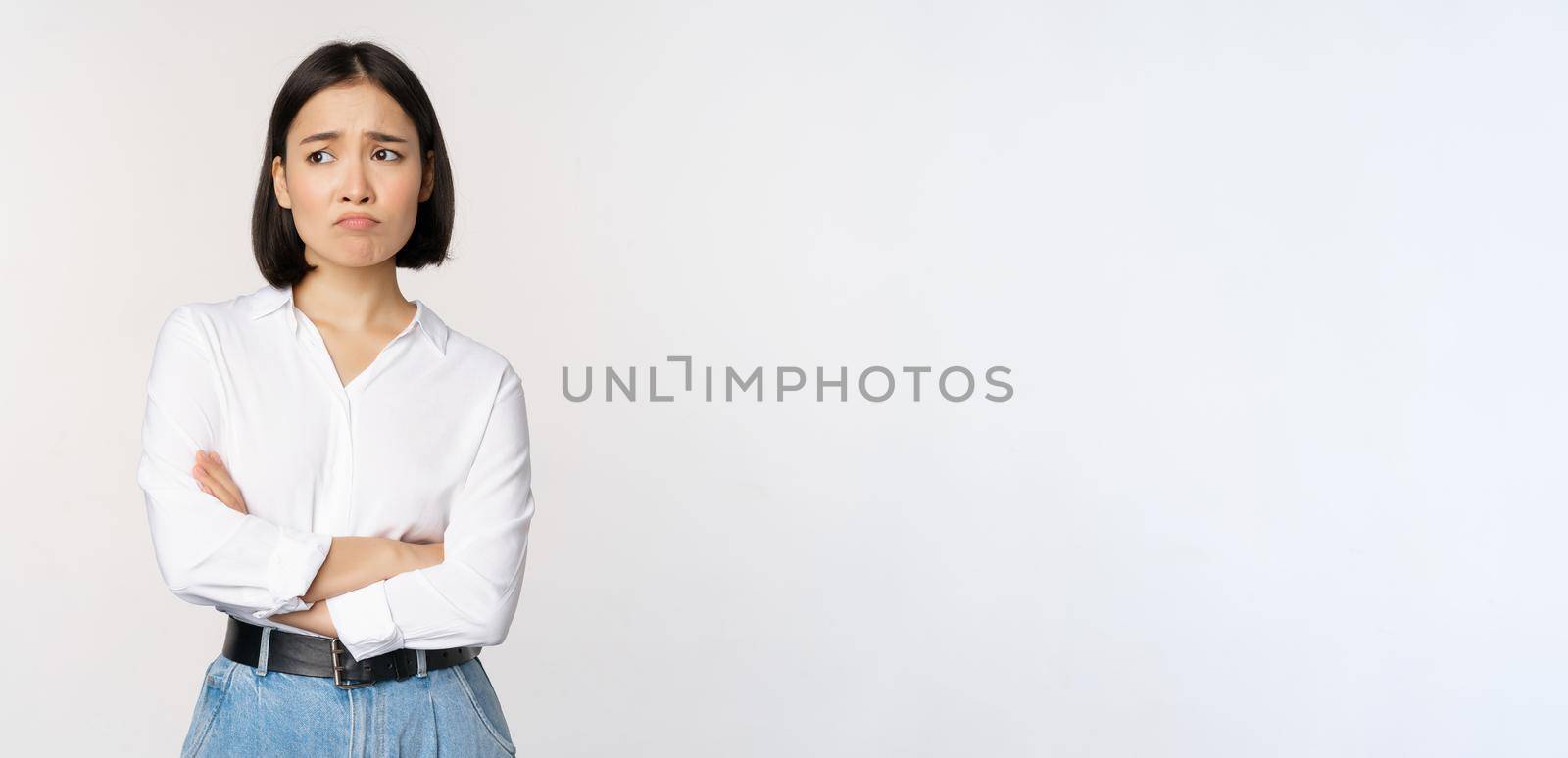 Image of sad office girl, asian woman sulking and frowning disappointed, standing upset and distressed against white background.