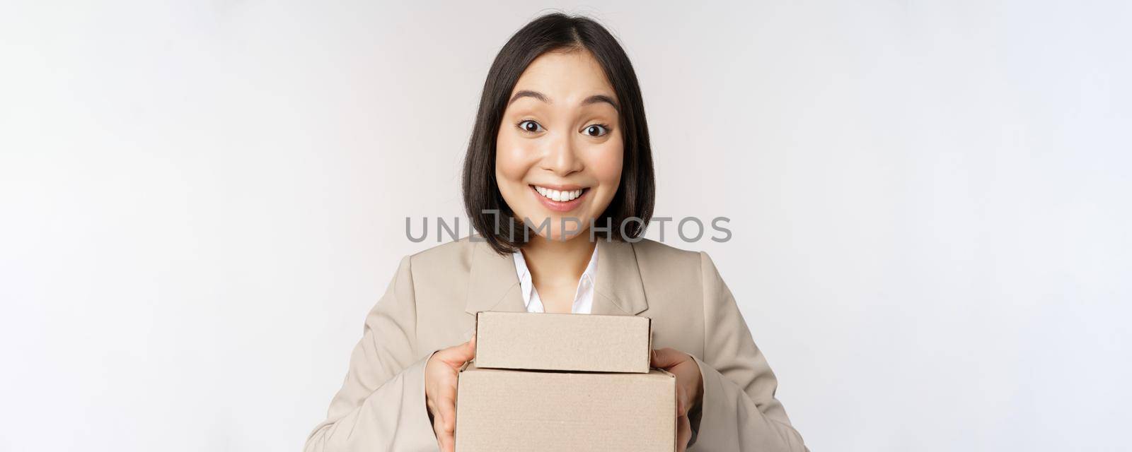 Image of asian saleswoman, business woman giving boxes with order, deliver to customer, standing in suit over white background by Benzoix
