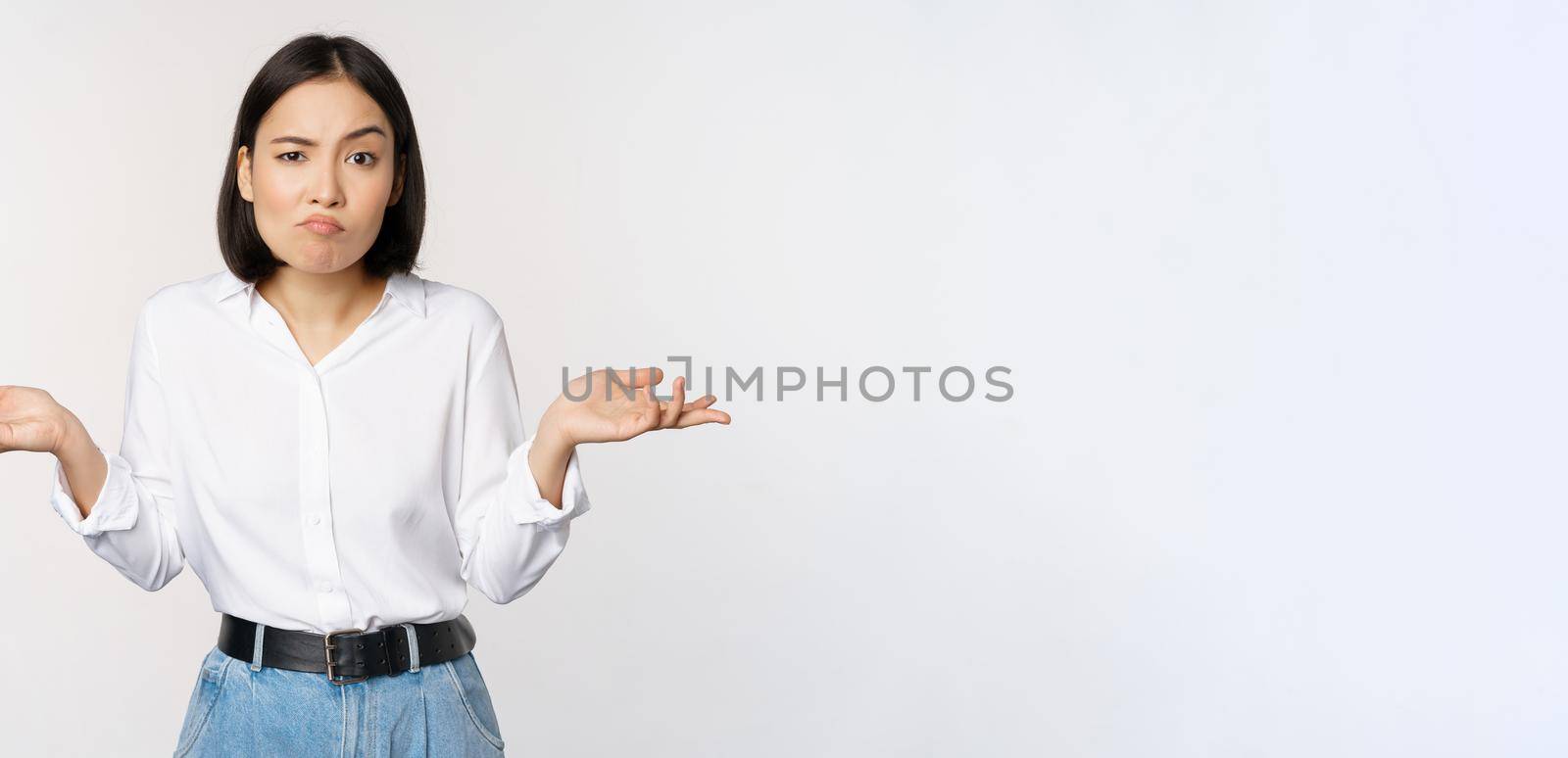 Image of confused asian office manager, office lady shrugging shoulders and looking clueless, standing puzzled against white background.