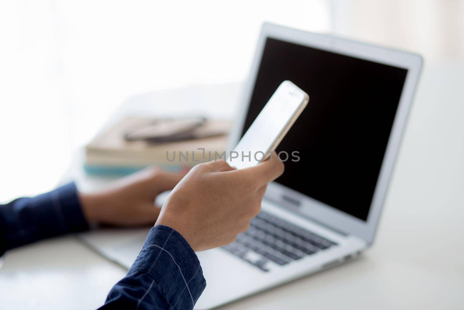 Hand of young man working with laptop computer and smartphone mockup on desk at home, notebook and phone display blank screen, freelance look message to internet, business and communication concept.