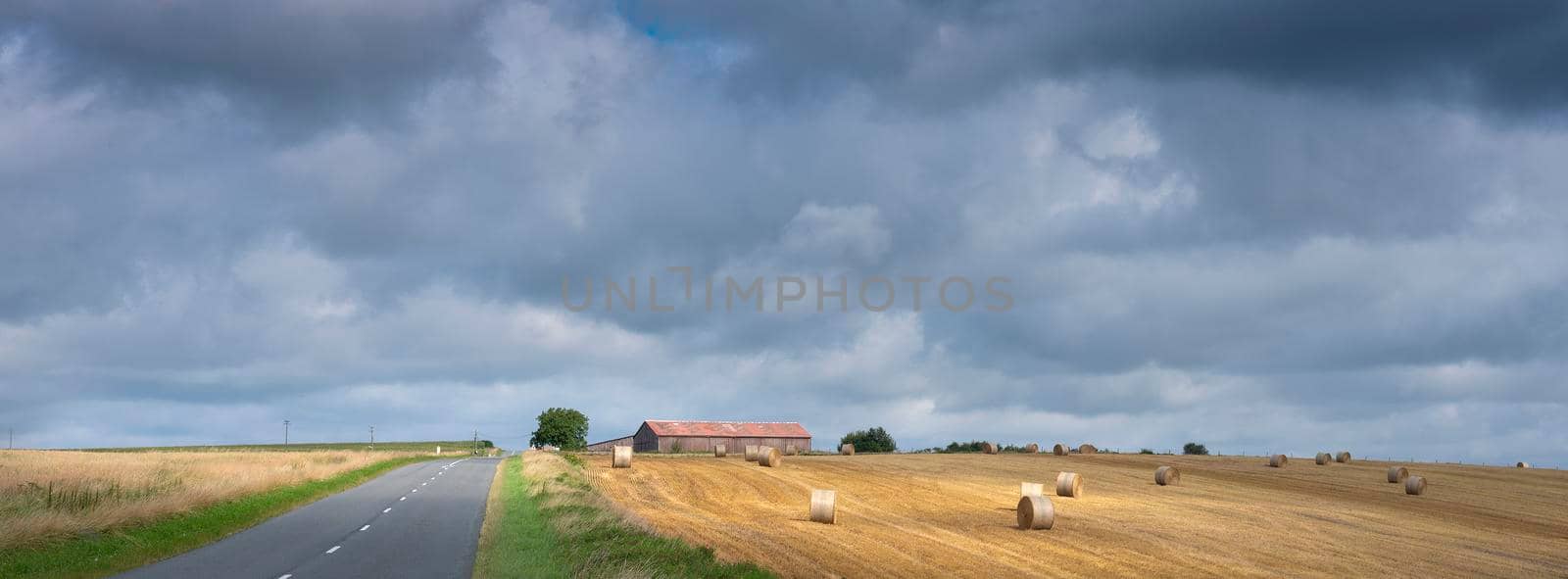 cloudy sky and summer countryside landscape with straw bales and barn in french ardennes near charleville