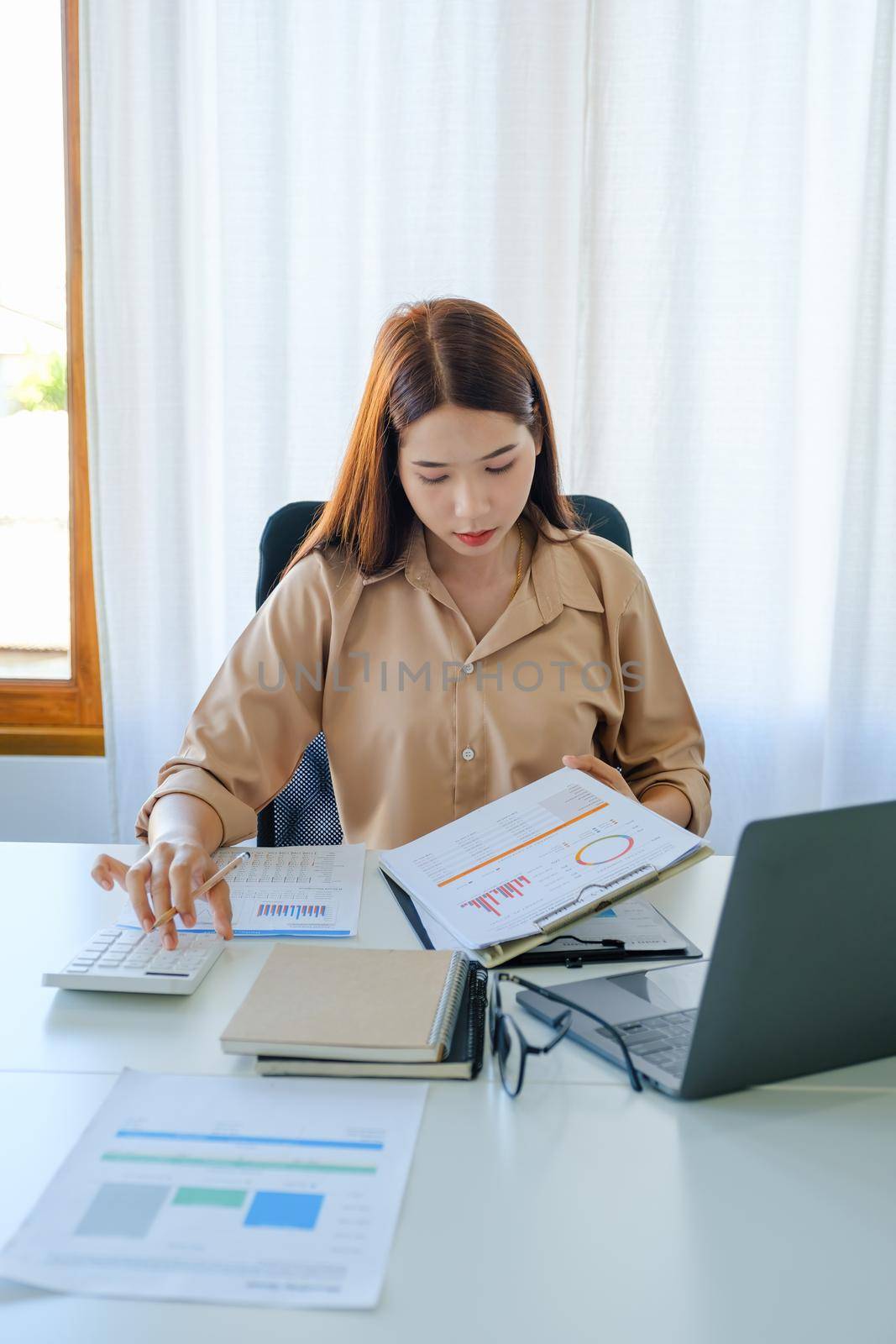 A female company employee is using a calculator to calculate sales income on a tablet computer screen via the Internet. by Manastrong