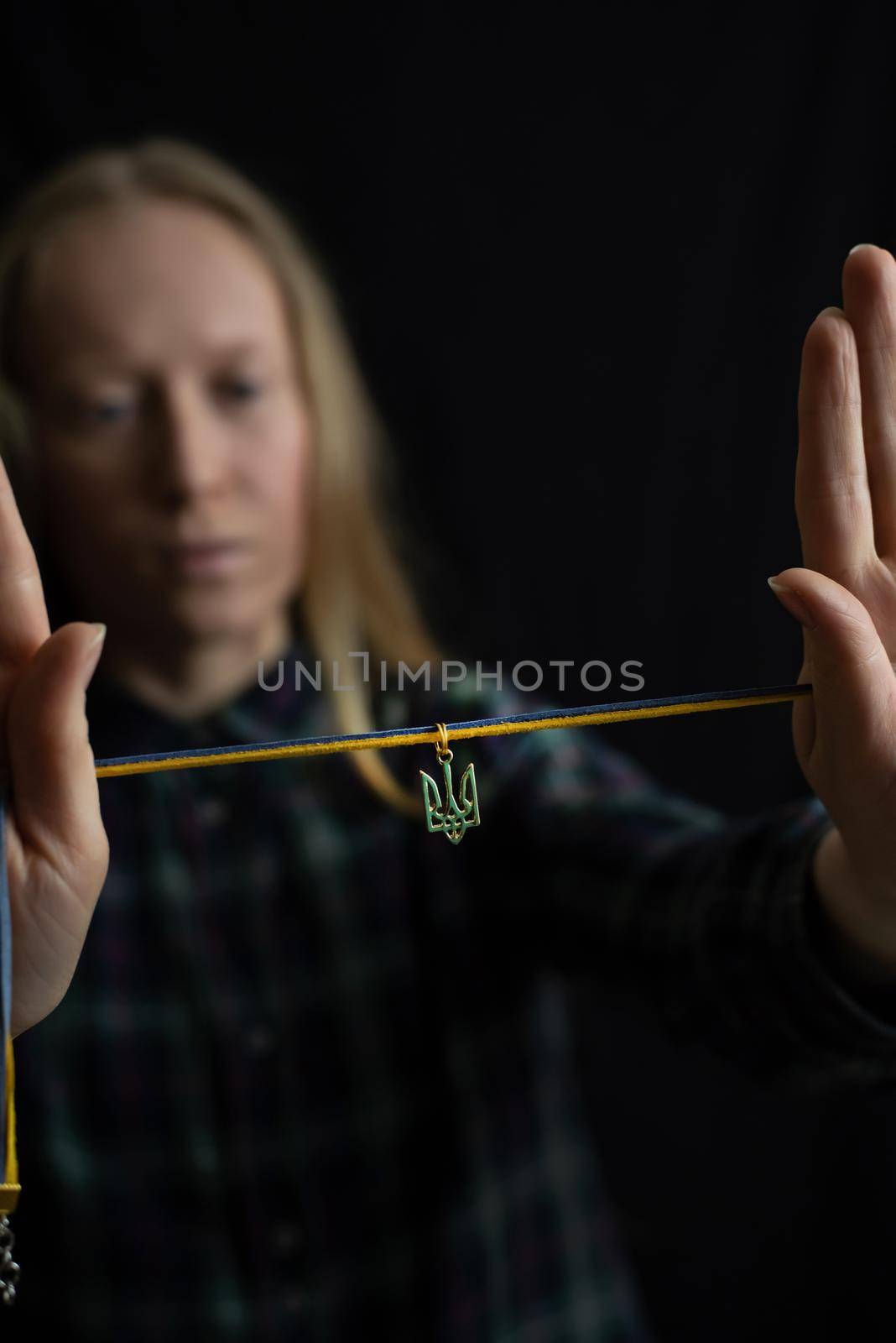 Ukrainian young blonde woman holding a pendant with the state emblem of Ukraine - Trident close up. Russia attacked Ukraine on February 24, 2022