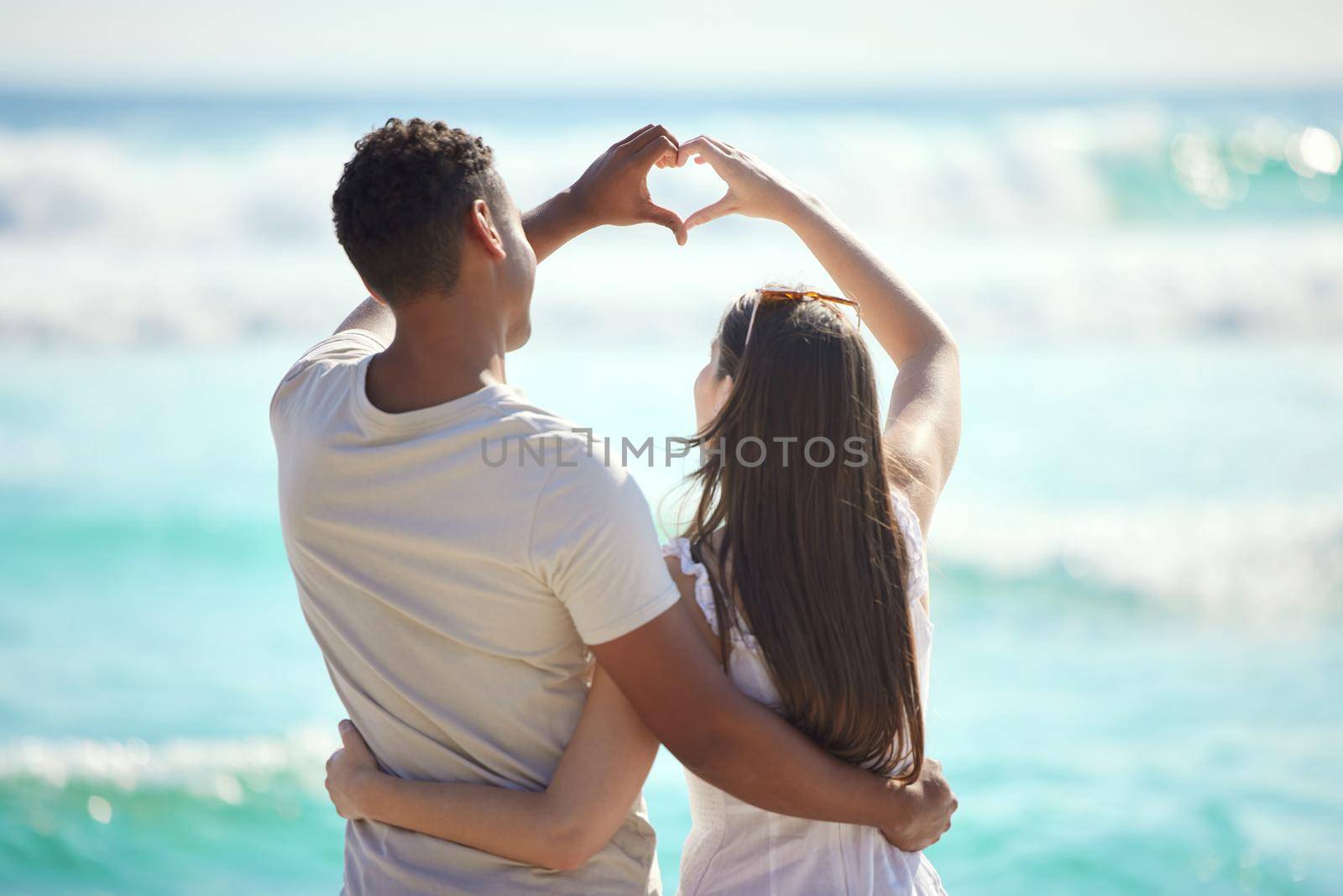 Shot of a young couple making a heart gesture with their hands at the beach.