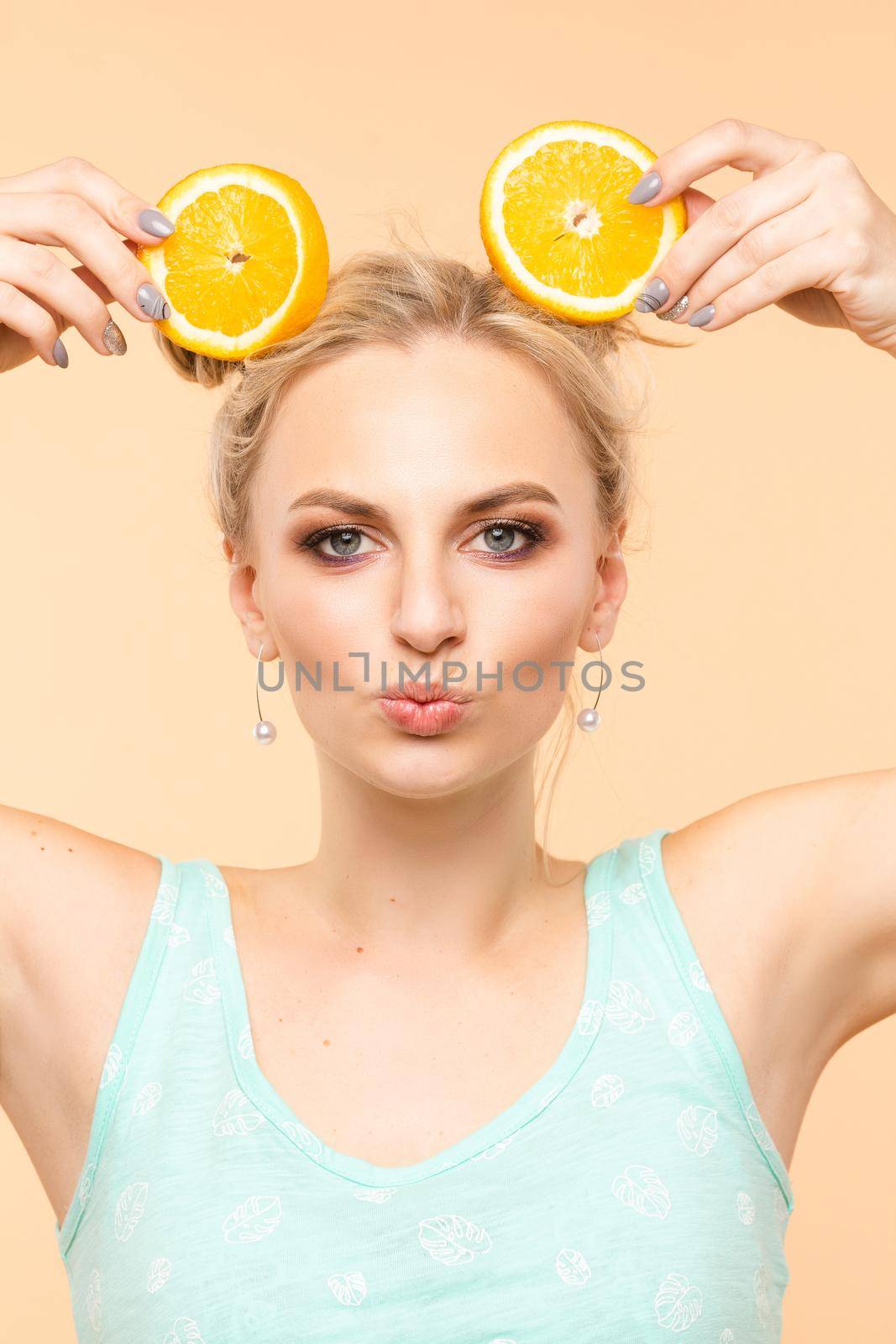 A beautiful sweet charming fresh bright woman with a cool hairstyle holds 2 orange slices in her hands, summer, joy, brightness copy space for advertisement by StudioLucky