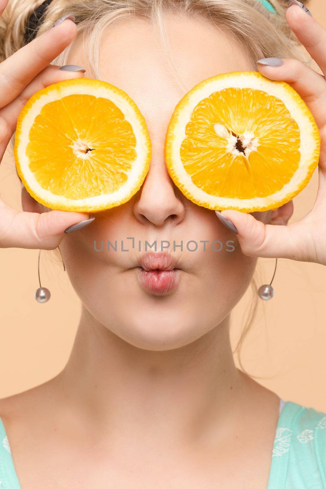 Pretty charming joyful attractive cheerful funny comic positive nude natural pure girl having two pieces of orange, closing one eye, isolated on beige background with copy space for advertisement