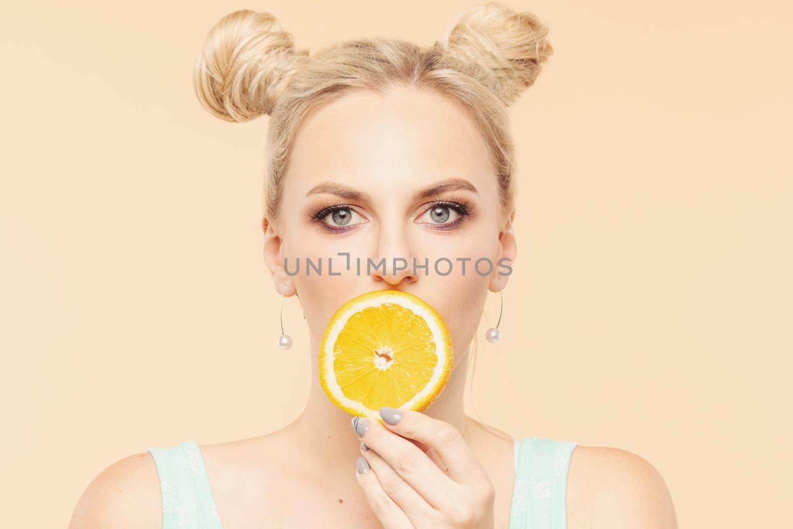Pretty charming joyful attractive cheerful funny comic positive nude natural pure girl having two pieces of orange, closing one eye, isolated on beige background with copy space for advertisement