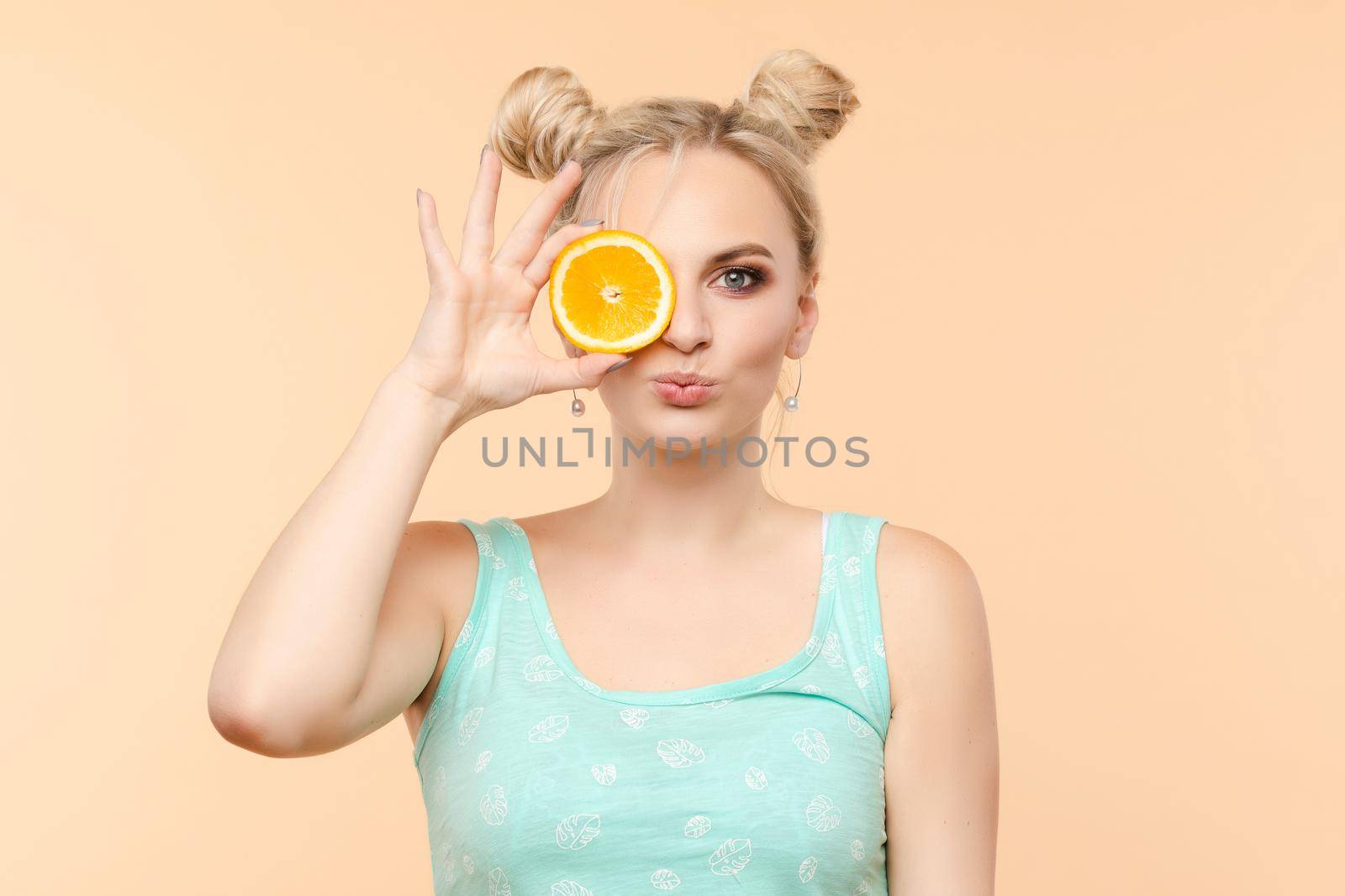 Pretty charming joyful attractive cheerful funny comic positive nude natural pure girl having two pieces of orange, closing one eye, isolated on beige background with copy space for advertisement