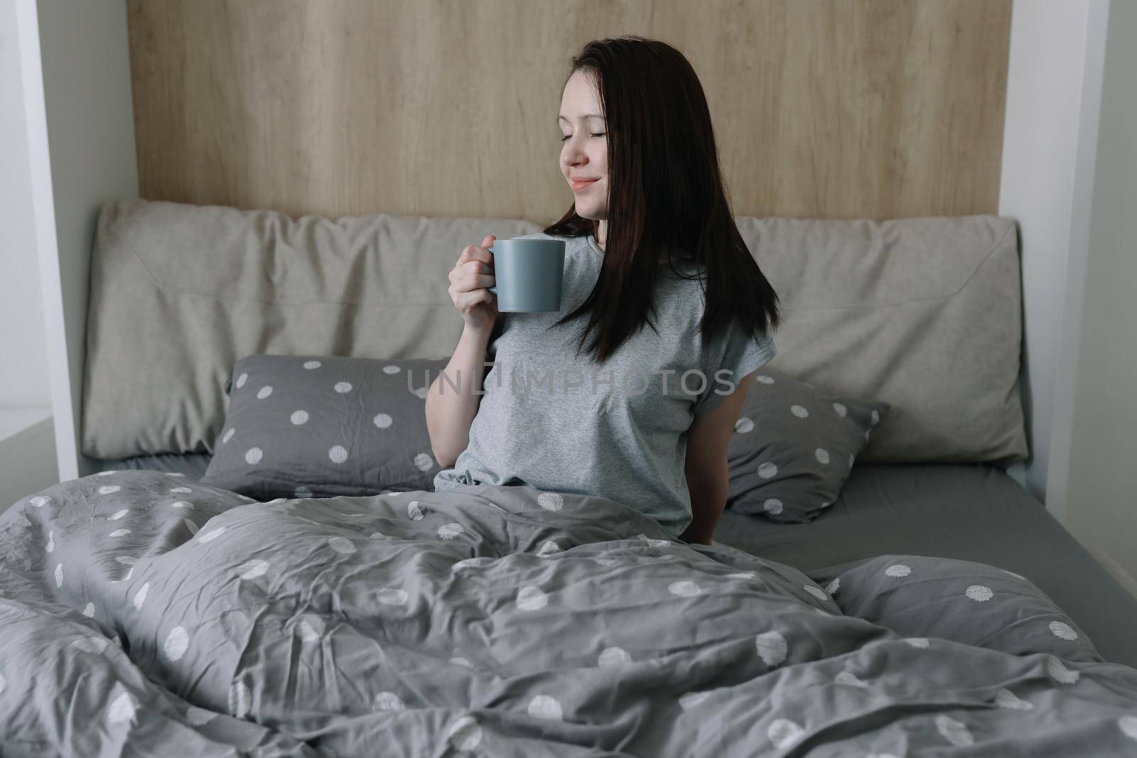 morning, coziness, cozy home concept - a young woman with cup of coffee or cacao in bed at home.