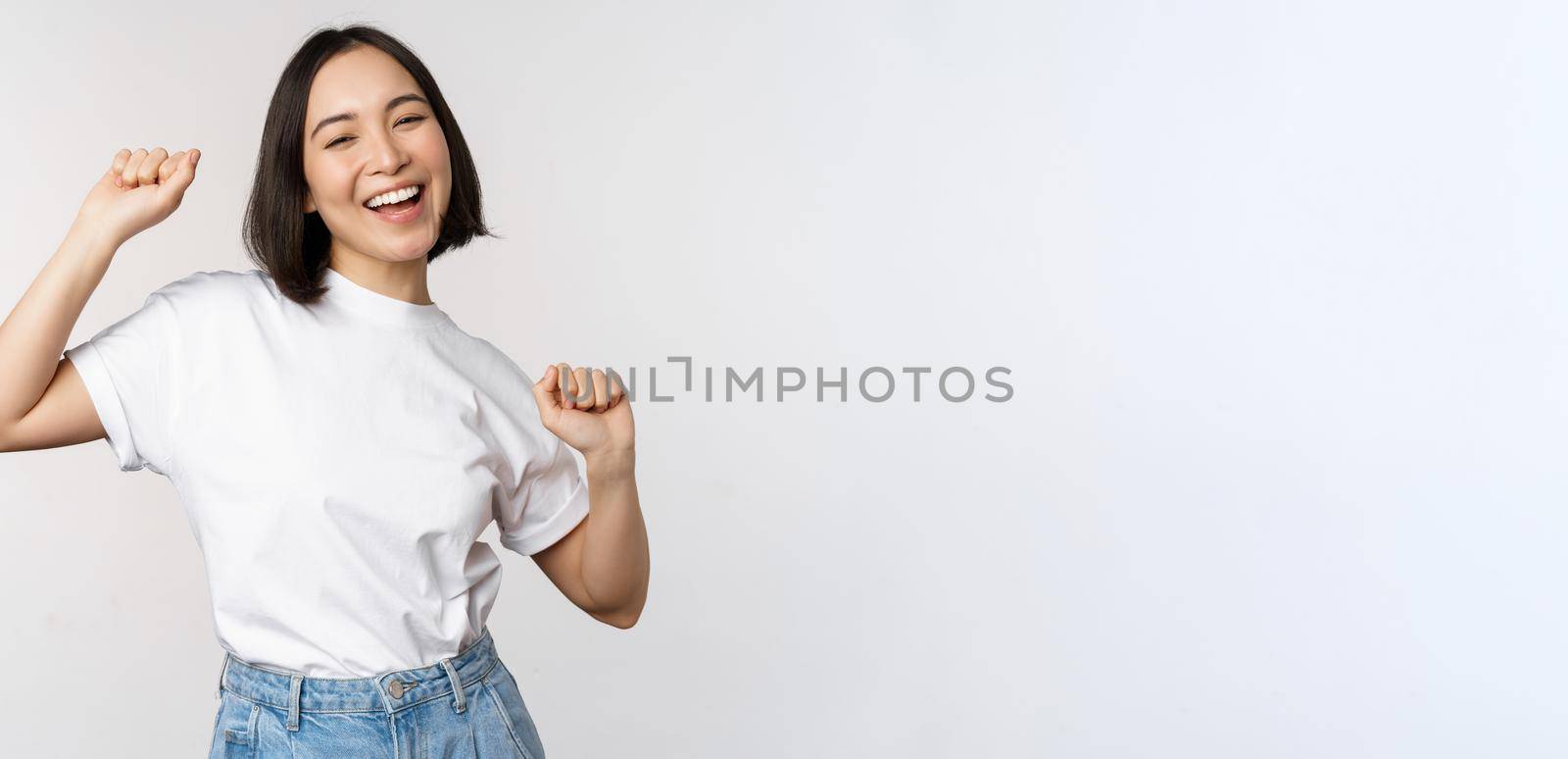 Happy dancing korean girl posing against white background, wearing tshirt by Benzoix