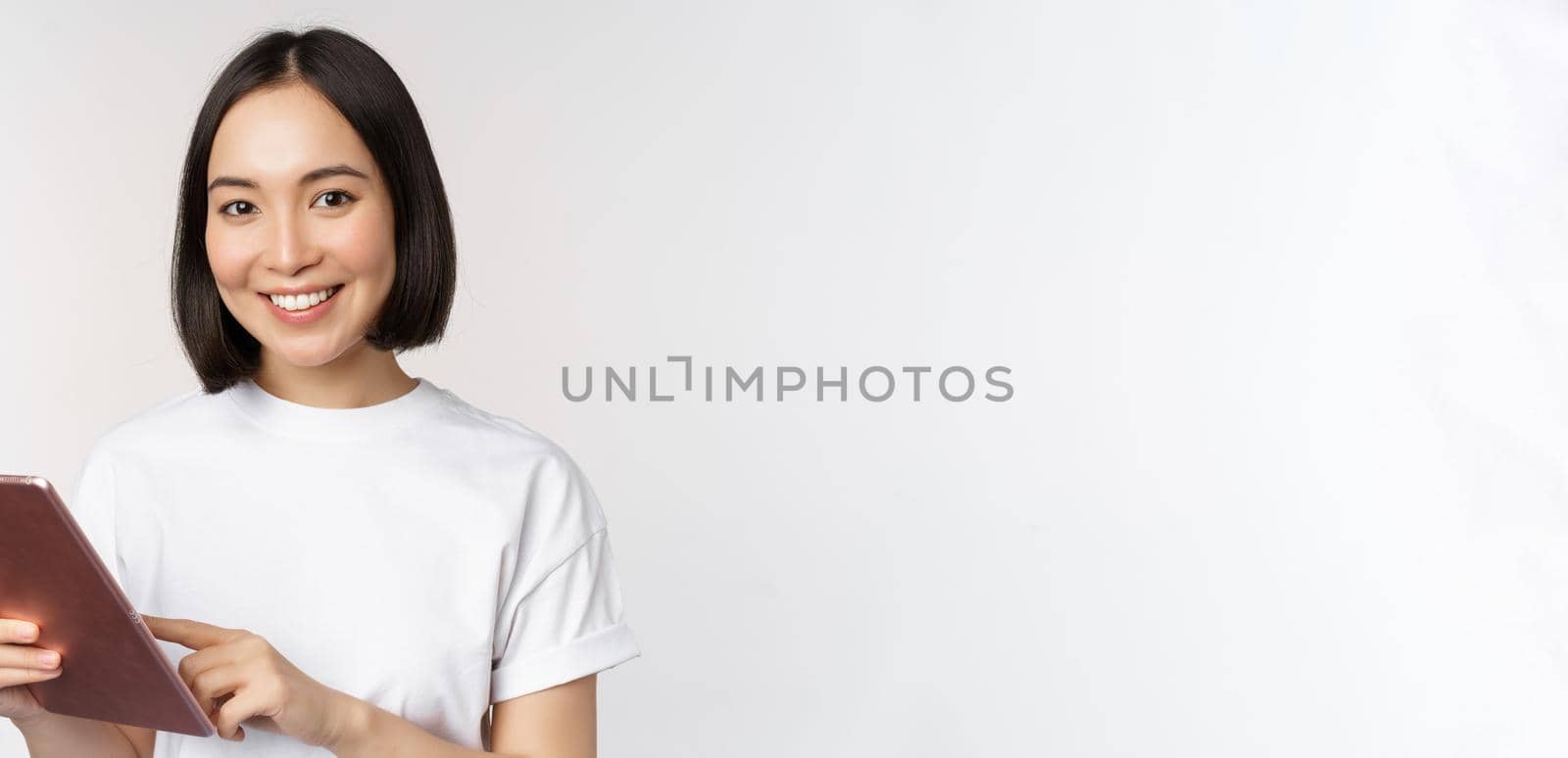 Asian girl using digital tablet, working with gadget, shopping online, standing over white background.