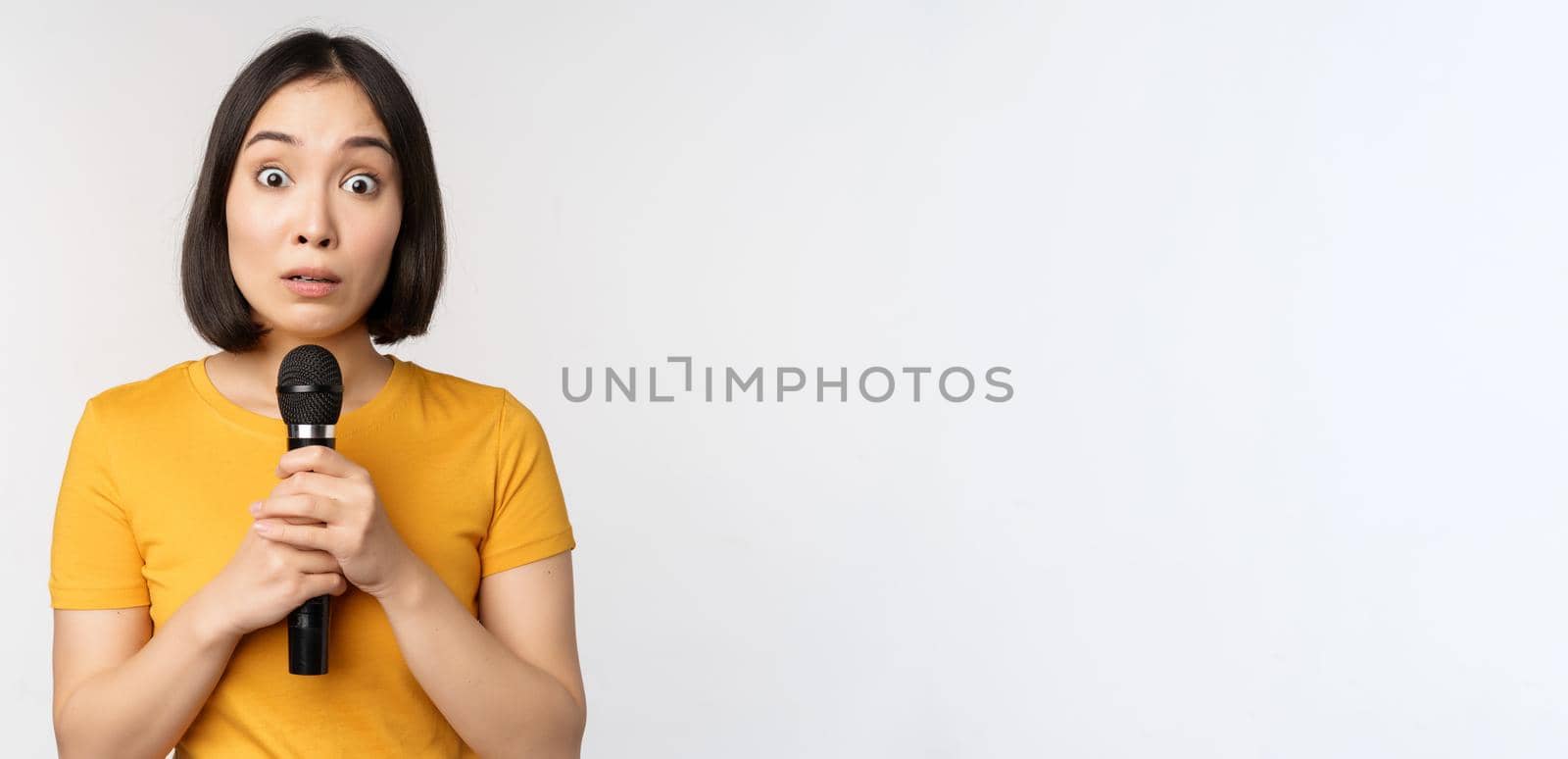 Modest asian girl holding microphone, scared talking in public, standing against white background by Benzoix