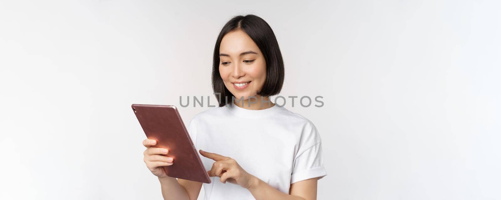 Asian girl using digital tablet, working with gadget, shopping online, standing over white background.