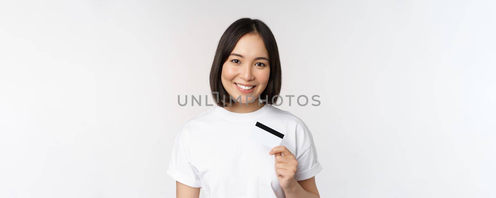 Portrait of korean smiling girl, bank client, showing credit card with happy face, standing against white background by Benzoix