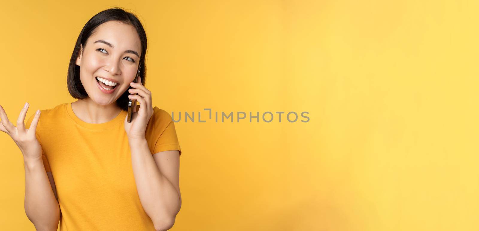 Young korean girl talking on mobile phone. Asian woman calling on smartphone, standing over yellow background.